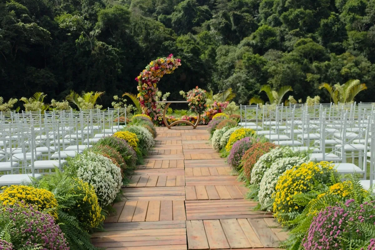 Passarela de madeira entre canteiros de flores, com as cadeiras da cerimônia